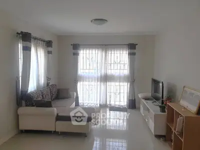 Bright living room with modern sofa and TV unit, featuring large windows and elegant curtains.