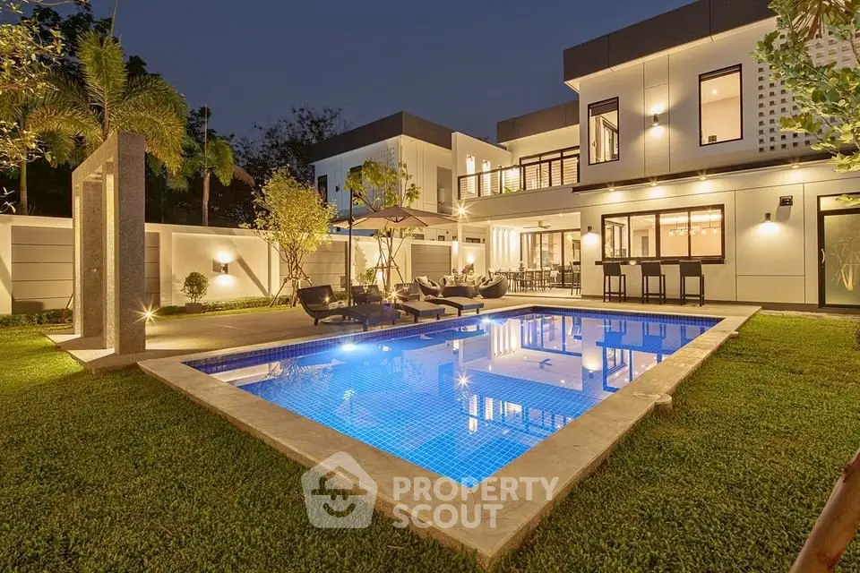 Luxurious modern home with illuminated pool and lush garden, perfect for evening relaxation.