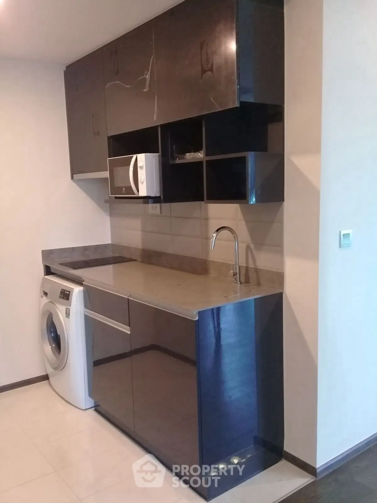 Modern kitchen with sleek cabinets, washing machine, and microwave in compact layout.