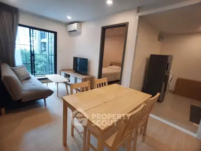 Modern open-plan living room with dining area and view into bedroom, featuring sleek furniture and natural light.
