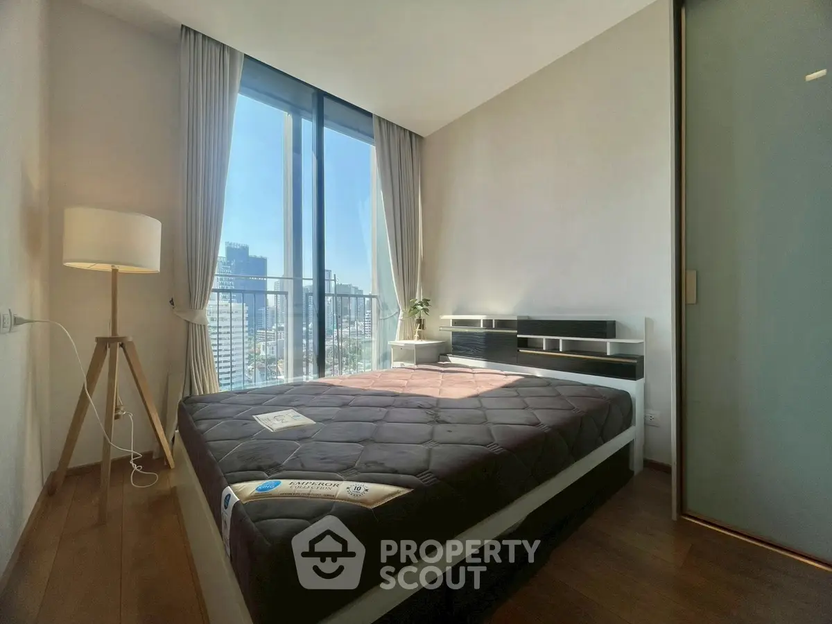 Modern bedroom with large window offering city view, featuring sleek furniture and natural light.