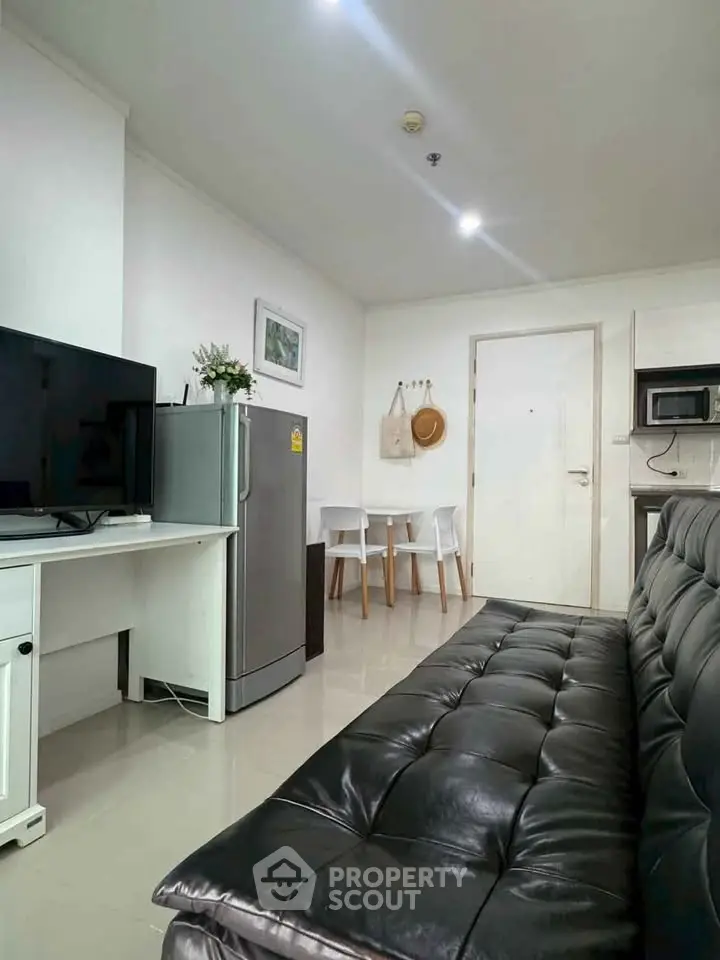 Modern living room with sleek black sofa, TV, and compact dining area in a cozy apartment.