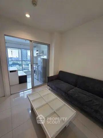 Modern living room with sleek sofa and glass coffee table, adjacent to a bright kitchen with city view.