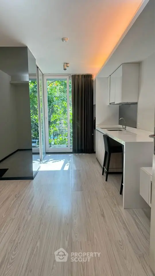 Modern studio apartment with sleek kitchen and large windows overlooking greenery.