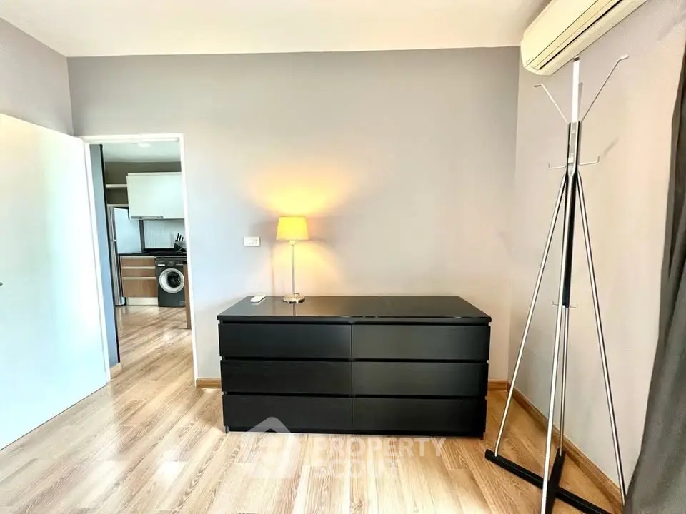 Modern bedroom with sleek black dresser and air conditioning, featuring a glimpse into a stylish kitchen.