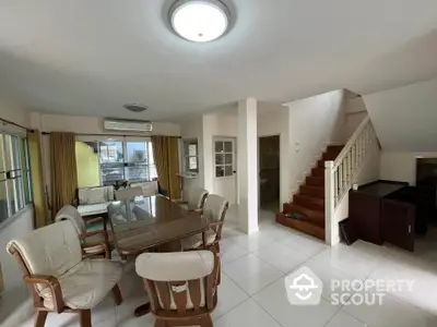 Spacious open-plan living room with dining area and staircase, featuring modern furniture and ample natural light.