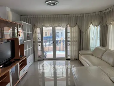 Spacious living room with elegant curtains and modern furniture, featuring a large window with balcony access.