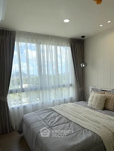 Cozy bedroom with large window and scenic view, featuring elegant curtains and plush bedding.