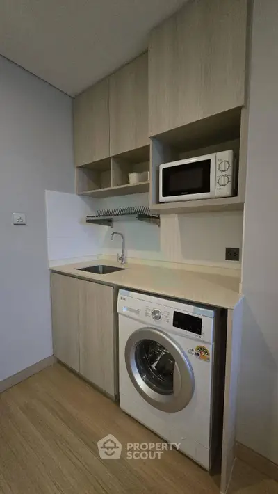 Compact modern kitchen with washing machine and microwave in sleek cabinetry.