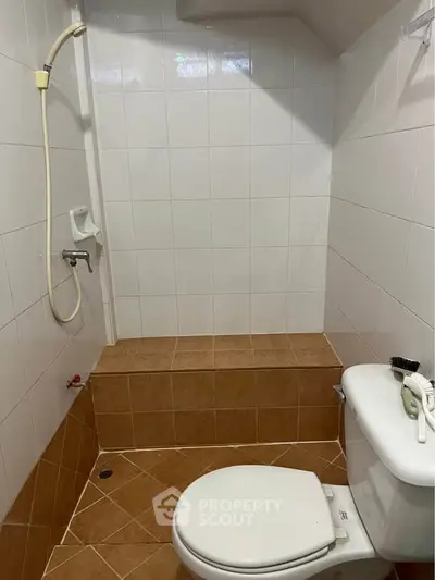 Compact bathroom with tiled walls and floor, featuring a toilet and shower area.