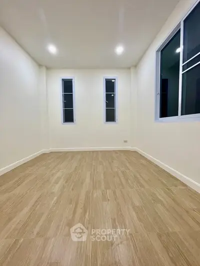 Spacious empty room with wooden flooring and large windows, perfect for customization.
