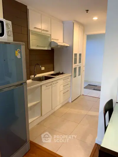 Modern compact kitchen with sleek white cabinetry and stainless steel appliances in a cozy apartment.