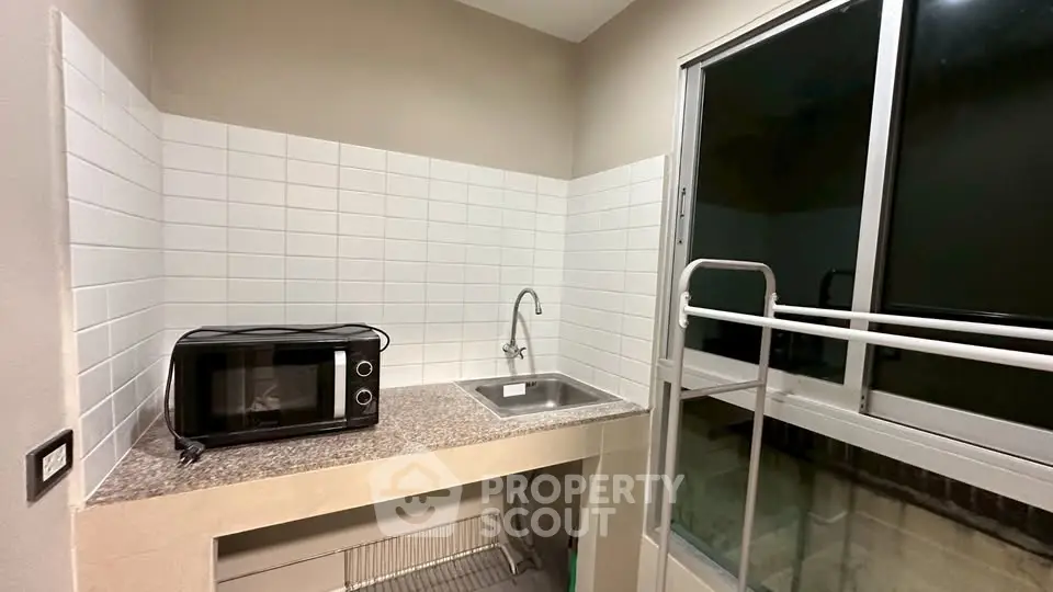 Compact kitchen with microwave and sink, featuring a sliding glass door for natural light.