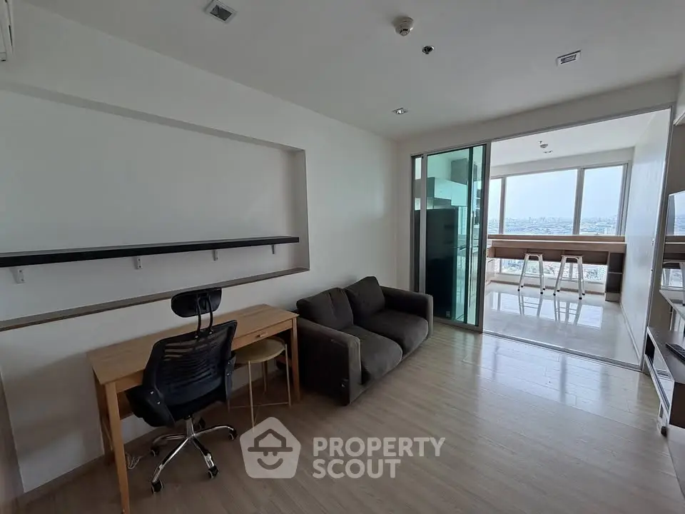 Modern living room with study area and city view, featuring sleek furniture and natural light.
