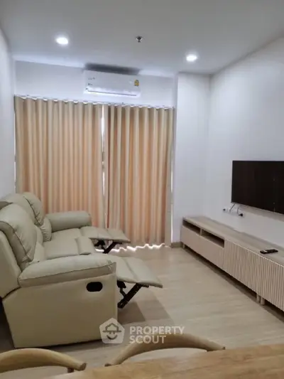 Spacious and well-lit living room with comfortable recliner sofa, modern entertainment unit, and elegant beige curtains complementing the neutral color palette.