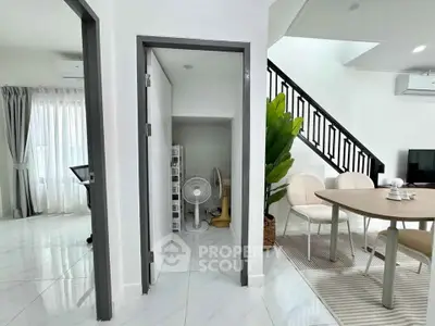 Modern open-plan living area with dining table and staircase, featuring sleek white interiors and natural light.