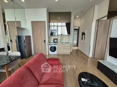 Modern apartment interior with red sofa, kitchen appliances, and wooden flooring.