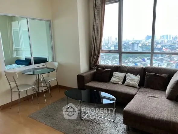 Modern living room with large windows and city view, featuring a cozy sectional sofa and glass coffee table.