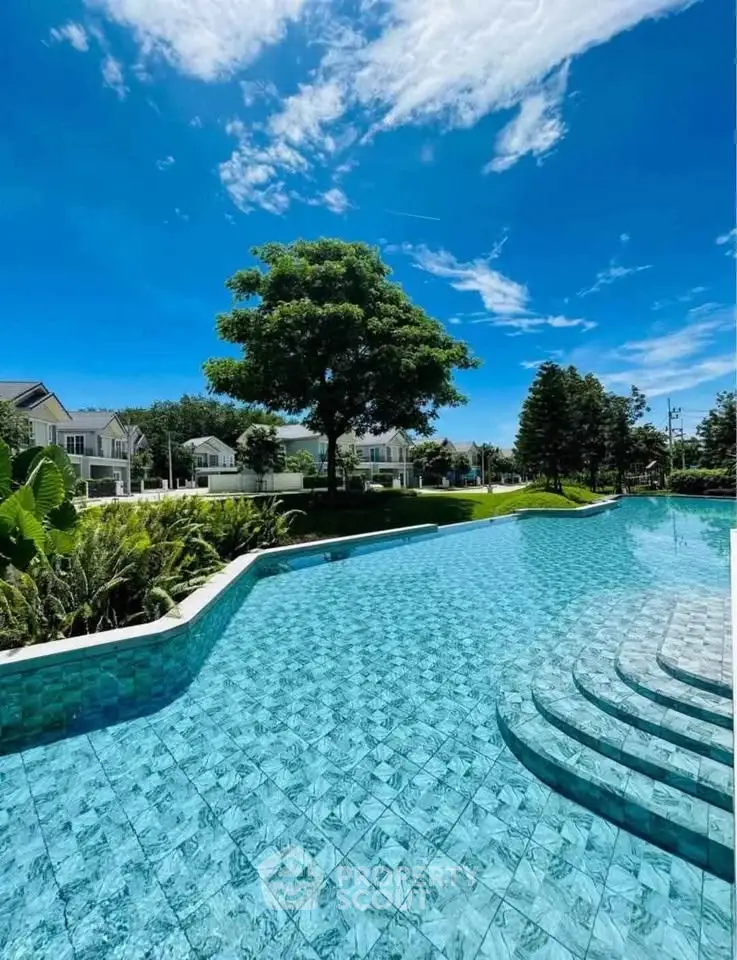 Luxurious residential pool with clear blue water and lush greenery under a bright sky.