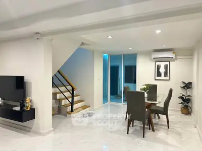 Modern living room with dining area, staircase, and sleek decor in a stylish home.