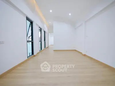 Spacious empty room with wooden flooring and large windows in modern apartment.