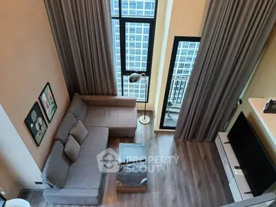 Modern living room with high ceilings and large windows offering city views, featuring a cozy gray sofa and stylish decor.