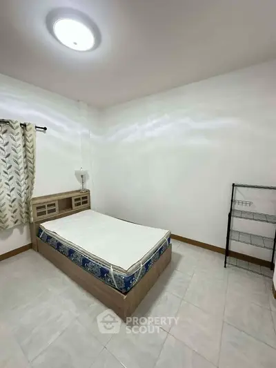 Spacious bedroom with minimalist decor and natural light, featuring a comfortable bed and tiled flooring.