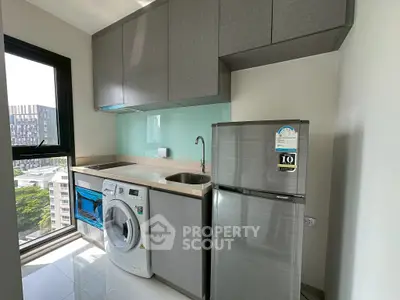 Modern kitchen with washing machine and fridge, featuring sleek cabinetry and a large window with city view.