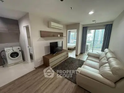 Modern living room with open layout, featuring a cozy sofa, TV, and washing machine, leading to a bedroom with city view.