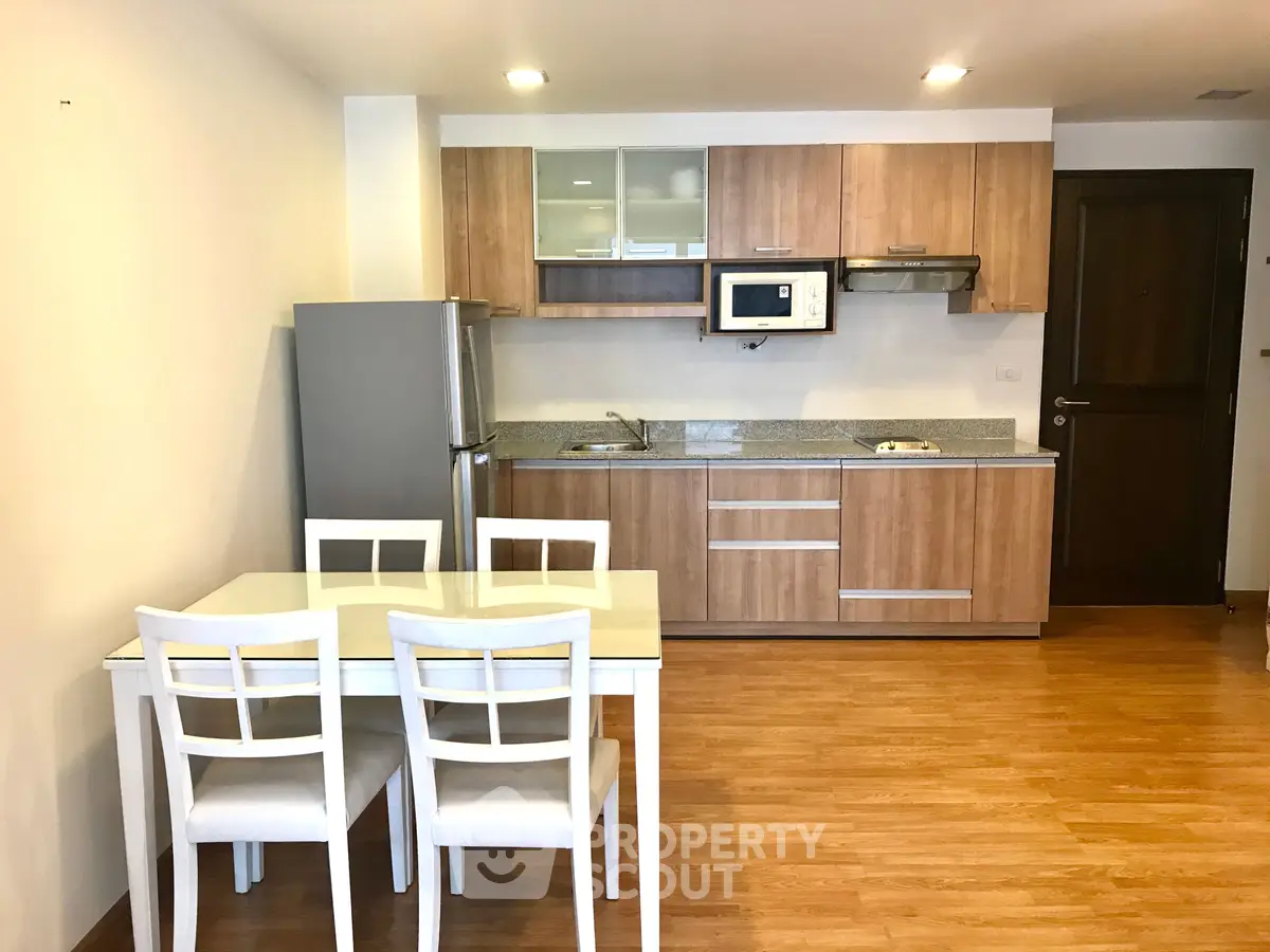 Modern kitchen with wooden cabinets, dining table, and stainless steel appliances in a cozy apartment.