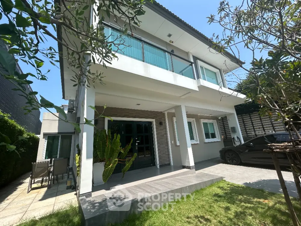 Spacious two-story home with large windows and a welcoming porch, nestled in a lush green garden, offering a serene suburban living experience.
