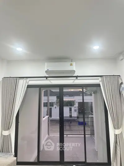 Modern living room with sliding glass doors leading to a balcony, featuring elegant curtains and a sleek air conditioning unit.