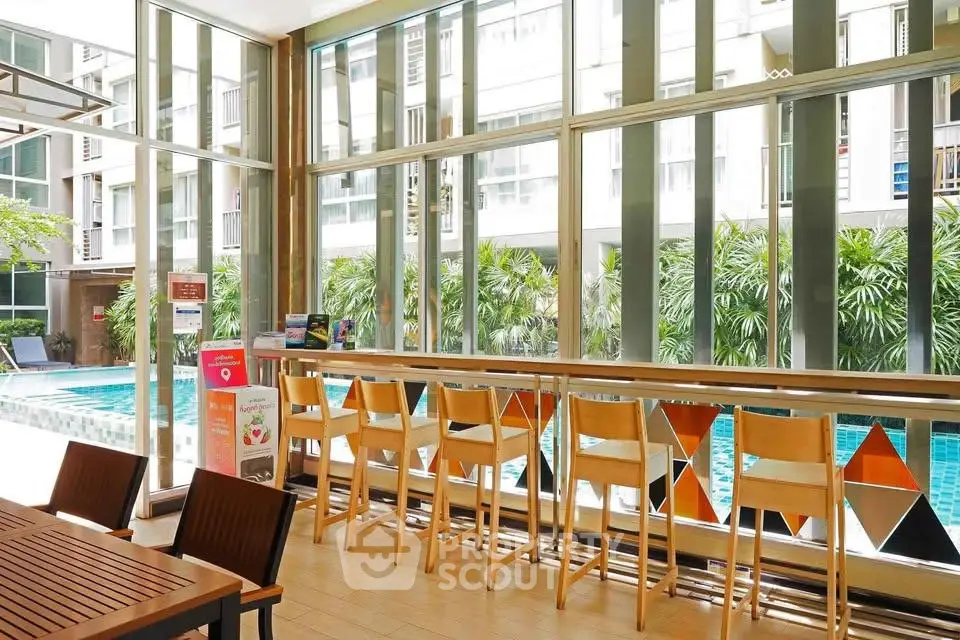 Modern poolside seating area with stylish bar stools and large windows overlooking lush greenery.