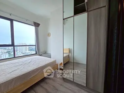 Modern bedroom with large window and mirrored wardrobe offering city views.