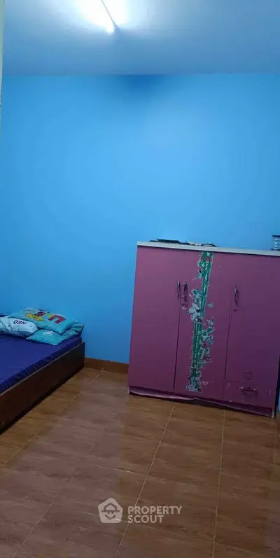 Cozy bedroom with vibrant blue walls and a pink wardrobe, perfect for a child's room.