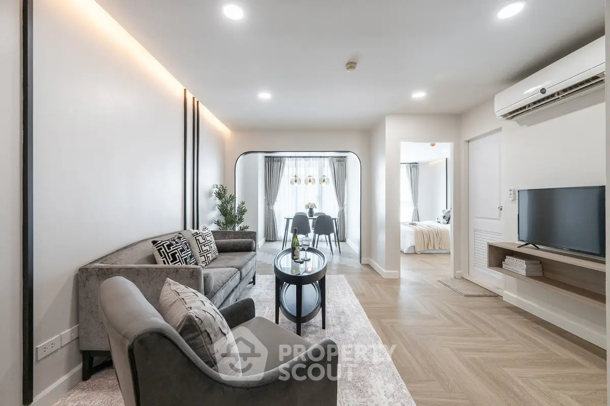 Modern living room with elegant decor and open layout leading to dining area and bedroom.