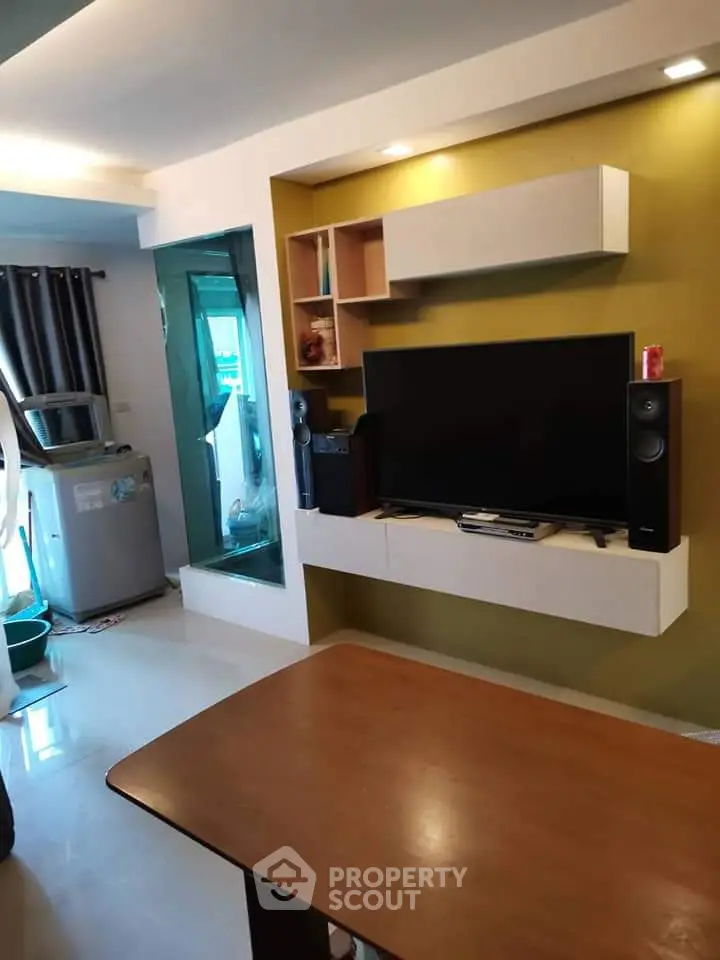 Modern living room with sleek TV setup and washing machine corner in stylish apartment.