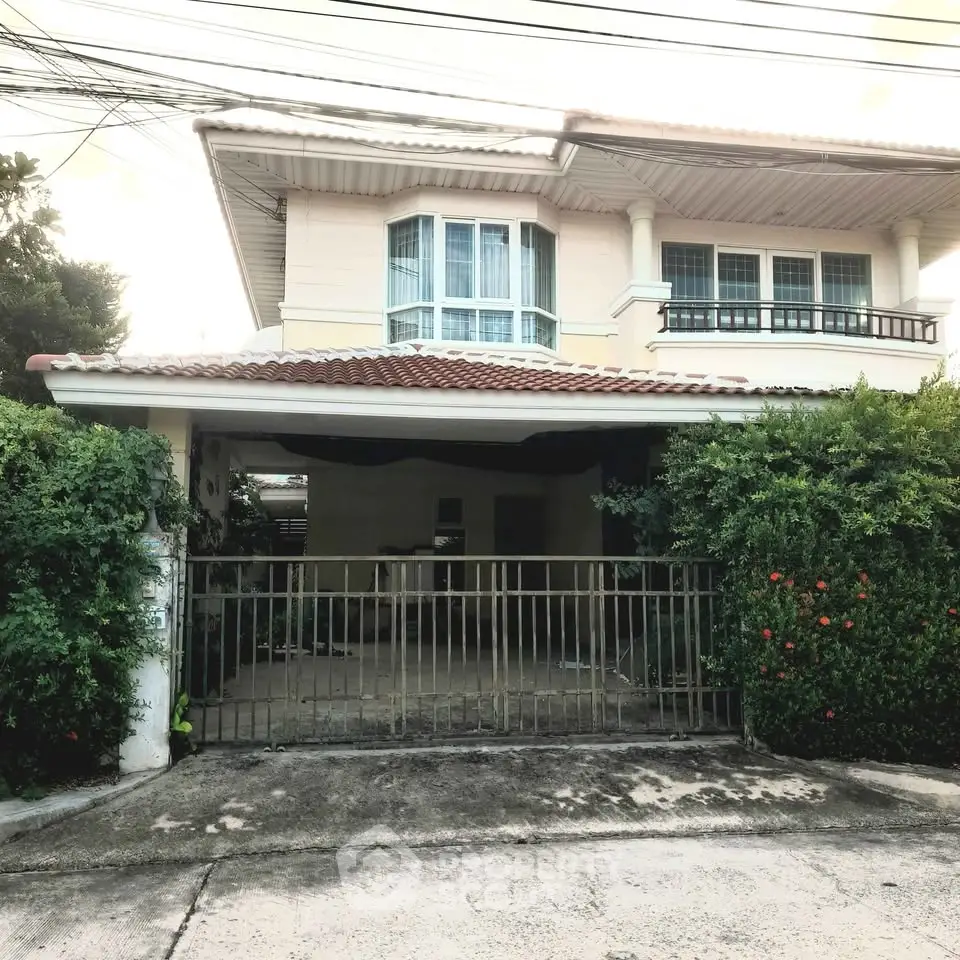 Charming two-story house with lush greenery and gated entrance, perfect for family living.