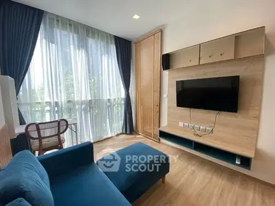 Modern living room with blue sofa, wall-mounted TV, and large windows with curtains.
