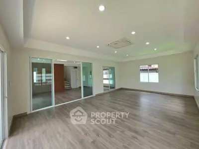 Spacious empty room with wooden flooring and large windows, perfect for customization.