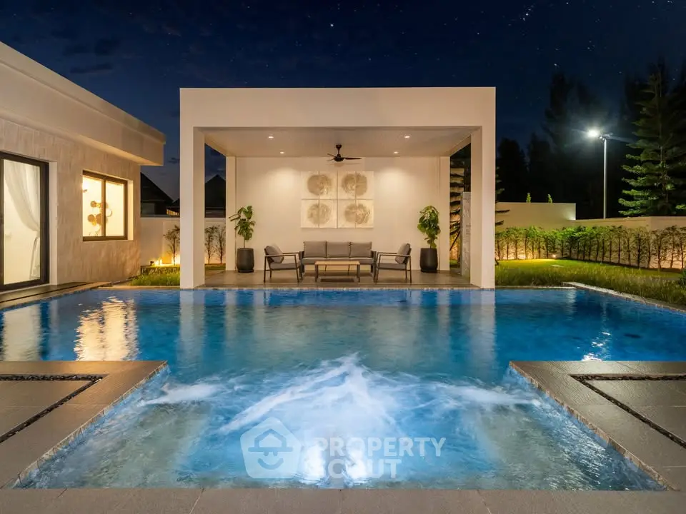 Luxurious modern home with illuminated pool and stylish outdoor seating area at night.