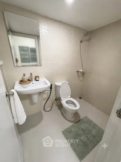 Modern bathroom with sleek fixtures and neutral tiles, featuring a wall-mounted sink and shower area.