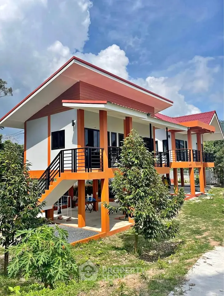 Modern two-story house with vibrant orange accents and lush greenery, perfect for family living.