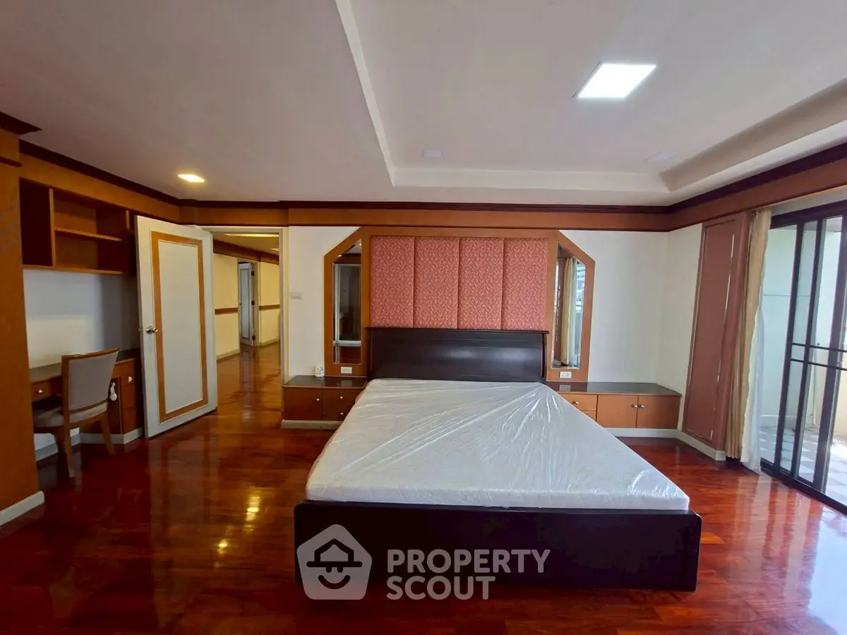 Spacious bedroom with elegant wooden flooring and large windows for natural light.