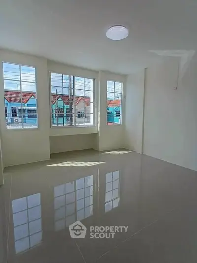 Bright empty room with large windows and glossy tiled floor, offering a view of colorful townhouses.
