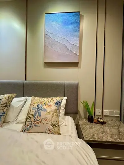 Elegant bedroom with stylish decor and modern artwork above the bed, featuring floral pillows and a marble side table.
