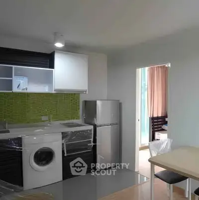 Modern kitchen with green backsplash, washing machine, and compact fridge in stylish apartment.
