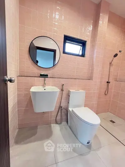 Modern bathroom with pink tiles, round mirror, and sleek fixtures.