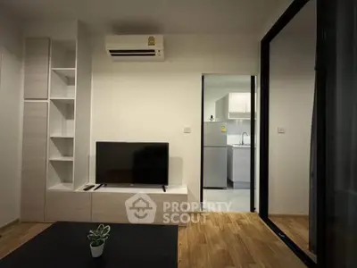 Modern living room with sleek TV setup and view into a contemporary kitchen.