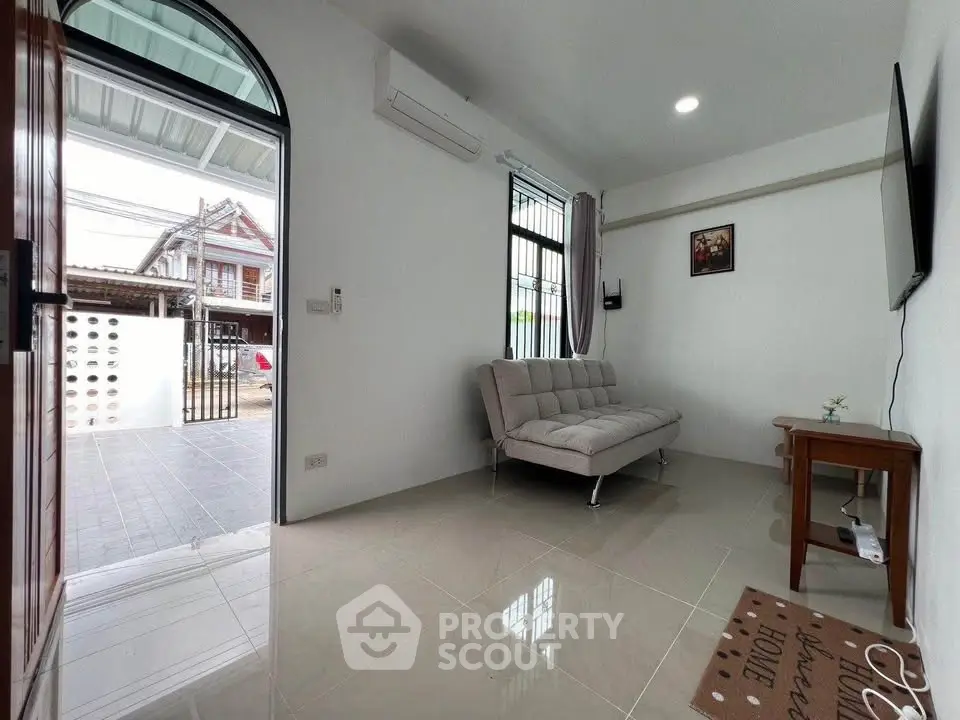 Modern living room with sleek sofa and wall-mounted TV, featuring a bright open entrance.